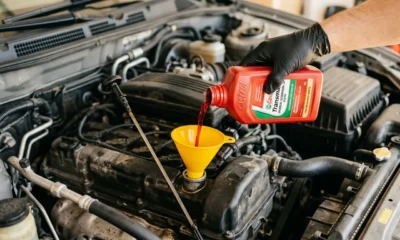3D photorealistic close-up of hand adding automatic transmission fluid through funnel into car engine bay with dipstick visible