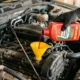 3D photorealistic close-up of hand adding automatic transmission fluid through funnel into car engine bay with dipstick visible